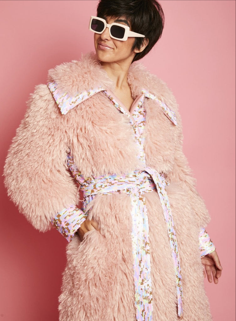 Person wearing a fluffy pink coat with a sequin belt against a pink background