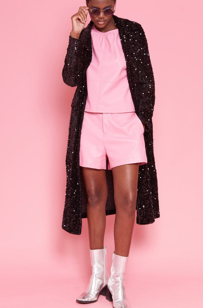 Person wearing a black sequin coat, pink outfit, and silver boots on a pink background