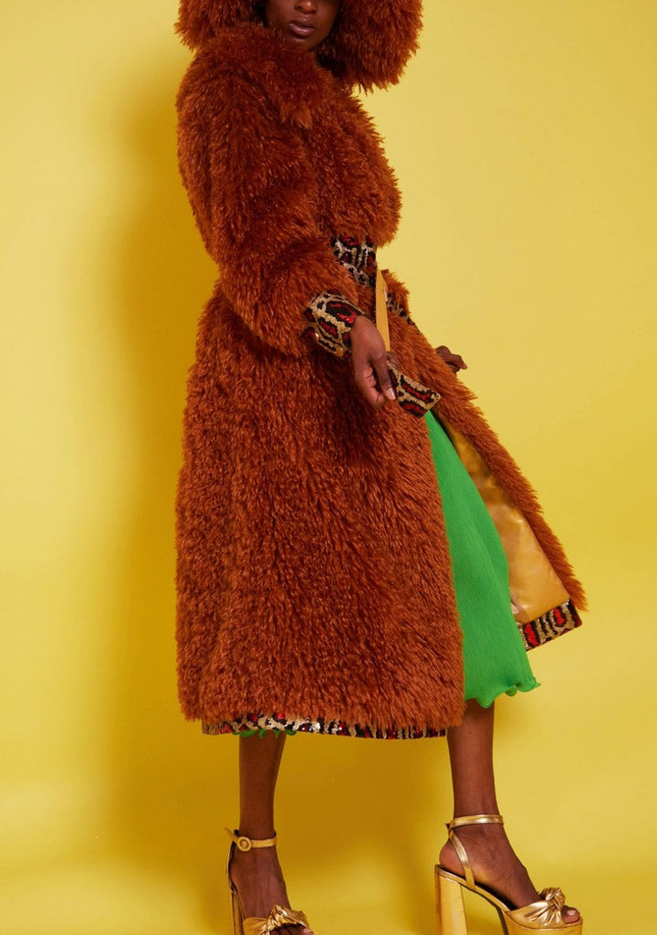 Person wearing a brown fluffy coat with a yellow background