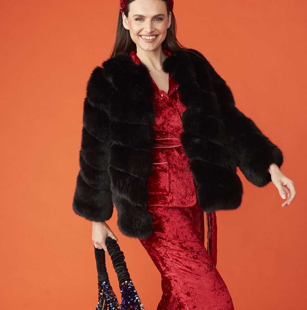 Woman wearing a red dress with a black fur coat against an orange background