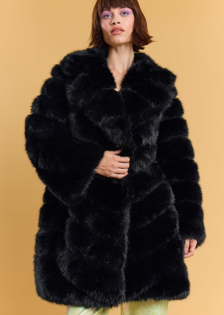 Woman wearing a black fur coat against a beige background