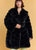 Woman wearing a black fur coat against a beige background