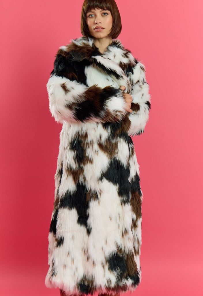 Person wearing a long, patterned fur coat against a pink background