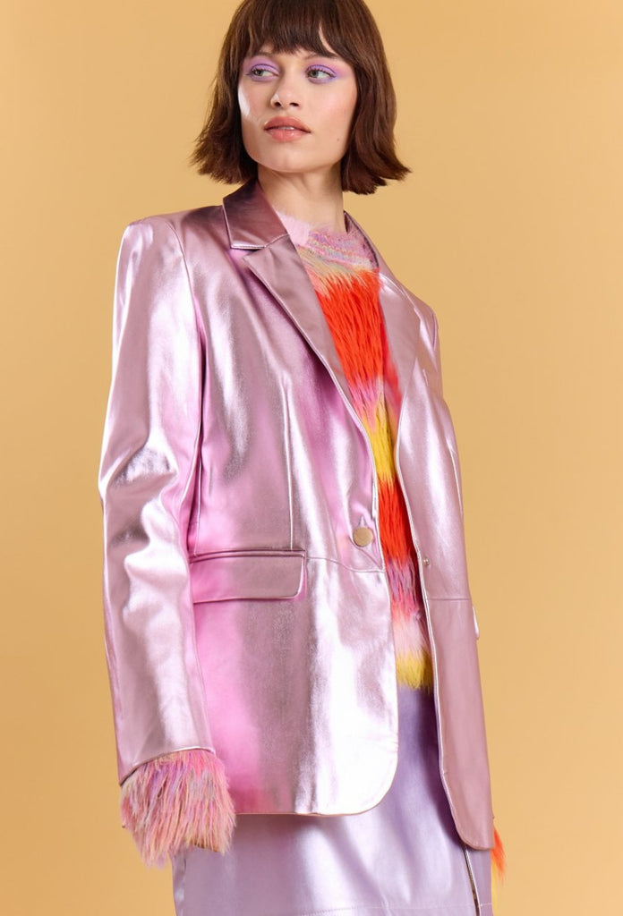 Woman wearing a pink satin blazer with colorful fringe details on a beige background