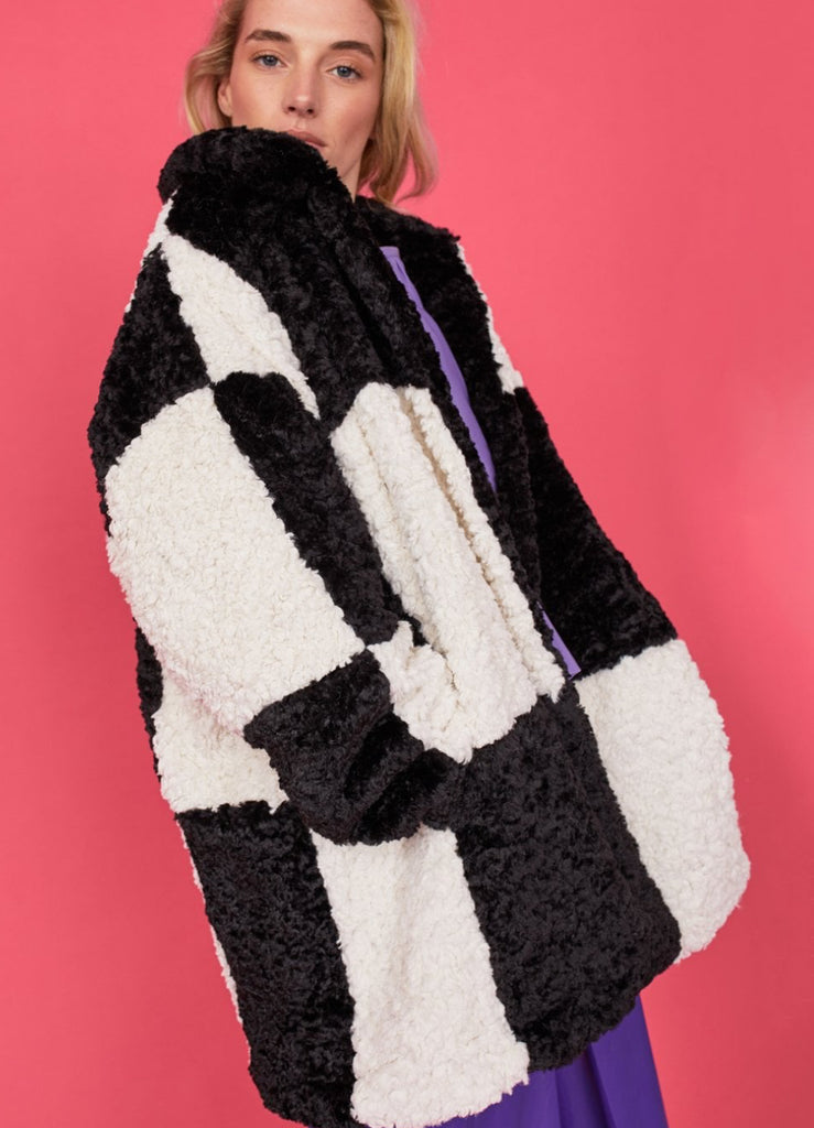 Person wearing a black and white checkered coat against a pink background